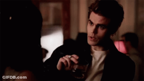 A Man Is Holding A Glass Of Wine And Smoking A Cigarette While Talking To A Woman . GIF