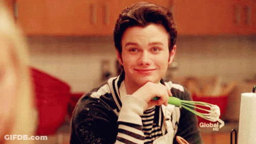 A Man Is Holding A Green Whisk In His Hand And Smiling In A Kitchen . GIF