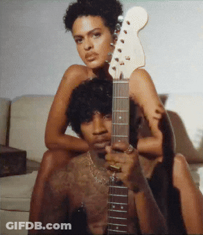 A Man Is Holding A Guitar With A Woman Sitting On His Back GIF
