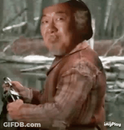A Man Is Holding A Gun And Making A Funny Face While Standing In The Woods . GIF