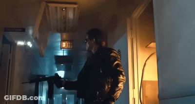 A Man Is Holding A Gun In A Dark Room With A Sign That Says Exit GIF