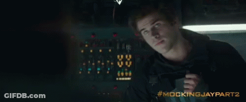 A Man Is Holding A Gun In A Dark Room With The Words Mockingjay Part 2 Written On The Bottom GIF