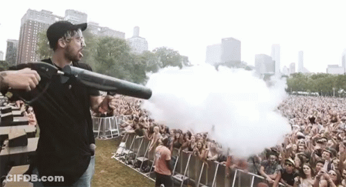 A Man Is Holding A Gun In Front Of A Crowd At A Concert GIF