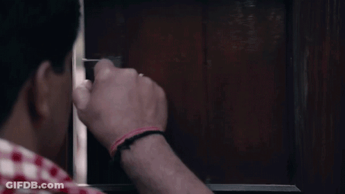 A Man Is Holding A Gun In His Hand And Looking Through A Window . GIF