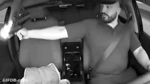 A Man Is Holding A Gun In His Hand While Sitting In A Car . GIF