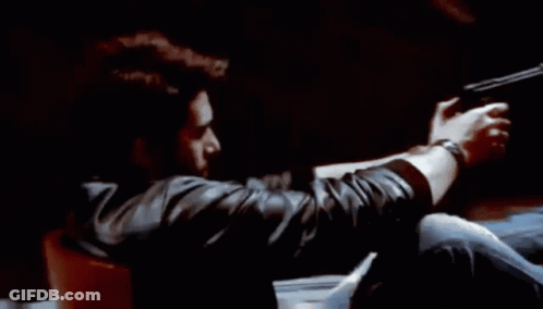 A Man Is Holding A Gun In His Hand While Sitting In A Chair . GIF