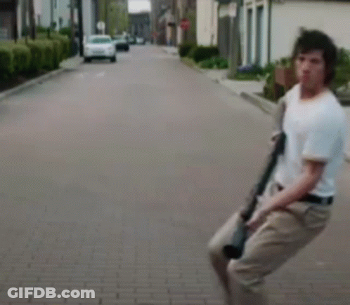 A Man Is Holding A Gun While Walking Down A Brick Street . GIF