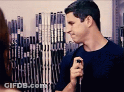 A Man Is Holding A Hockey Stick In Front Of A Wall Of Hockey Sticks GIF
