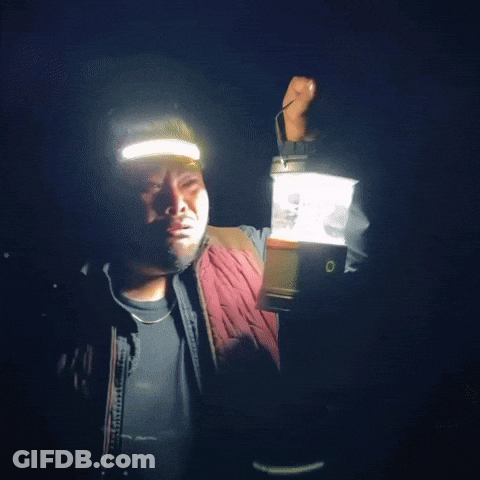 A Man Is Holding A Lantern In His Hand And Wearing A Headlamp GIF