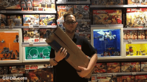 A Man Is Holding A Large Box In Front Of A Display Of Lego Star Wars And Ninjago Toys GIF
