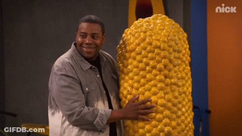 A Man Is Holding A Large Corn On The Cob In Front Of A Nick Sign GIF