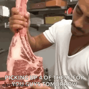 A Man Is Holding A Large Piece Of Meat In His Hands In A Kitchen . GIF