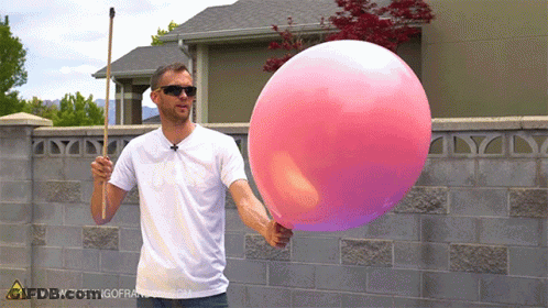A Man Is Holding A Large Pink Balloon In Front Of A Brick Wall GIF