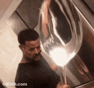 A Man Is Holding A Large Silver Balloon In His Hand . GIF