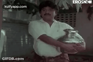 A Man Is Holding A Large Vase In His Hands . GIF