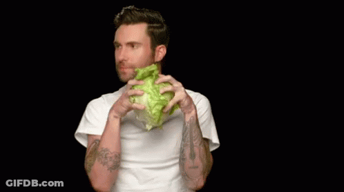 A Man Is Holding A Lettuce Head In Front Of His Mouth . GIF