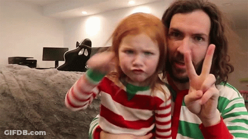 A Man Is Holding A Little Girl Who Is Making A Funny Face While Giving A Peace Sign . GIF
