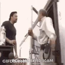 A Man Is Holding A Microphone And Talking To Another Man While Standing In Front Of A Truck . GIF