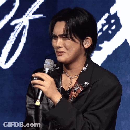 A Man Is Holding A Microphone In Front Of A Blue Background GIF