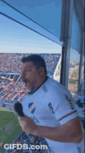 A Man Is Holding A Microphone In Front Of A Crowd At A Soccer Game .. GIF
