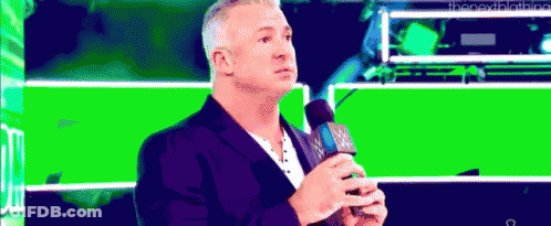 A Man Is Holding A Microphone In Front Of A Green Background . GIF