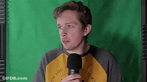 A Man Is Holding A Microphone In Front Of A Green Screen And Making A Funny Face . GIF