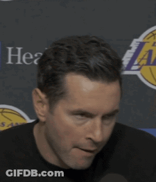 A Man Is Holding A Microphone In Front Of A Lakers Logo GIF