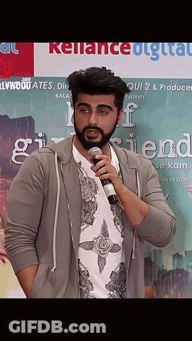 A Man Is Holding A Microphone In Front Of A Poster For Girlfriend GIF