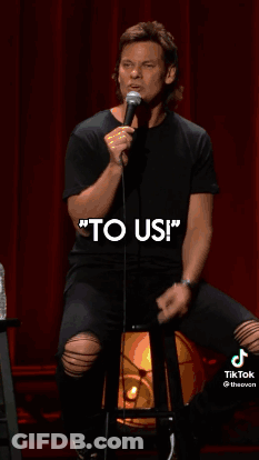 A Man Is Holding A Microphone In Front Of A Red Curtain And Talking Into It . GIF