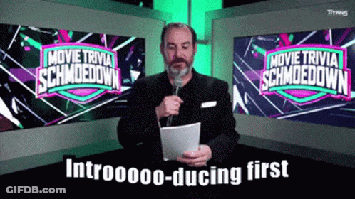 A Man Is Holding A Microphone In Front Of A Screen That Says Movie Trivia Schmoodown GIF