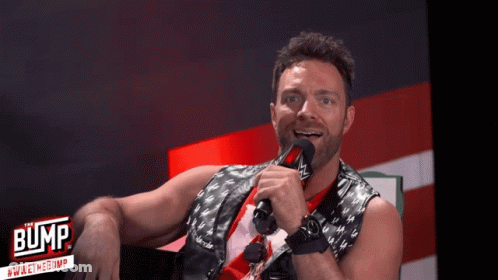 A Man Is Holding A Microphone In Front Of A Sign That Says " Bump " GIF