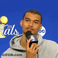 A Man Is Holding A Microphone In Front Of A Sign That Says Finals 2026 GIF