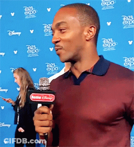 A Man Is Holding A Microphone In Front Of A Wall That Says Disney Expo GIF