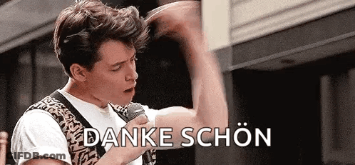 A Man Is Holding A Microphone In His Hand And Saying `` Danke Schön '' In German . GIF