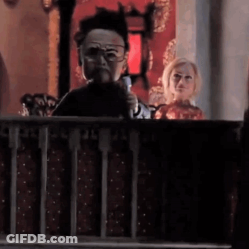A Man Is Holding A Microphone In His Hand While A Woman Looks On . GIF