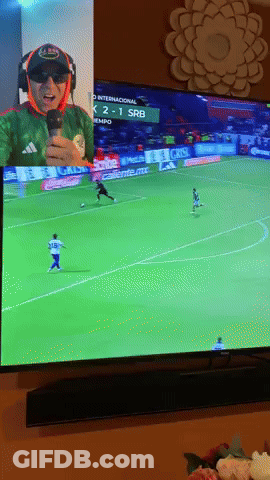 A Man Is Holding A Microphone While Watching A Soccer Game On A Tv GIF