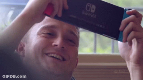 A Man Is Holding A Nintendo Switch In His Hand . GIF