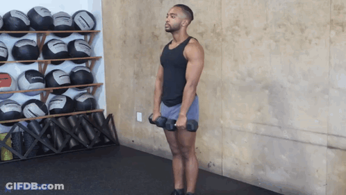 A Man Is Holding A Pair Of Dumbbells In Front Of A Wall With Balls On It GIF