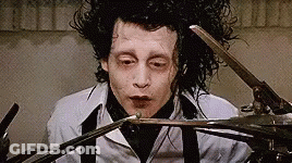 A Man Is Holding A Pair Of Scissors In His Hand . GIF