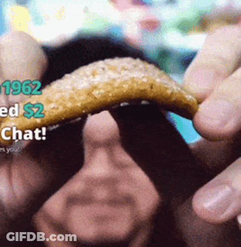 A Man Is Holding A Piece Of Food In His Hand With 1962 Ed $ 2 Chat On The Bottom GIF