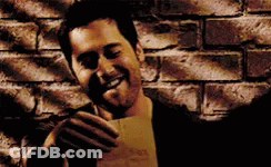 A Man Is Holding A Piece Of Paper In Front Of A Brick Wall And Smiling . GIF