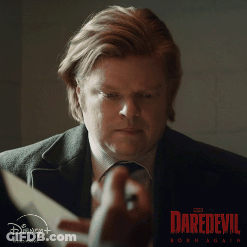 A Man Is Holding A Piece Of Paper In Front Of A Daredevil Born Again Poster GIF
