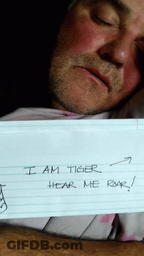 A Man Is Holding A Piece Of Paper That Says I Am Tiger Roar Hear Me GIF