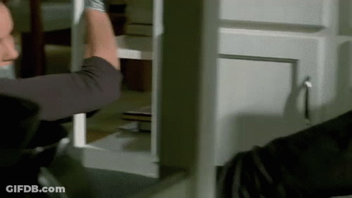 A Man Is Holding A Piece Of Wood In His Hand While Standing In Front Of A Cabinet . GIF