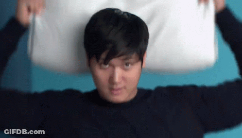 A Man Is Holding A Pillow Over His Head . GIF