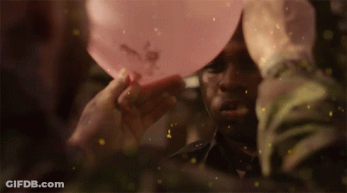 A Man Is Holding A Pink Balloon Over His Head With Flowers On It GIF