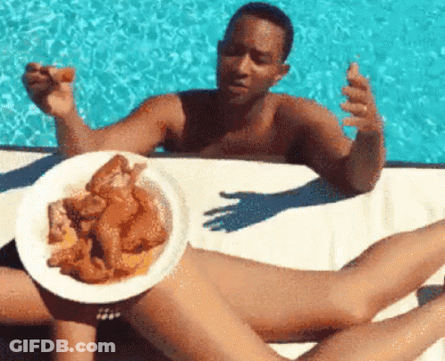A Man Is Holding A Plate Of Chicken Wings Over A Woman 'S Legs GIF