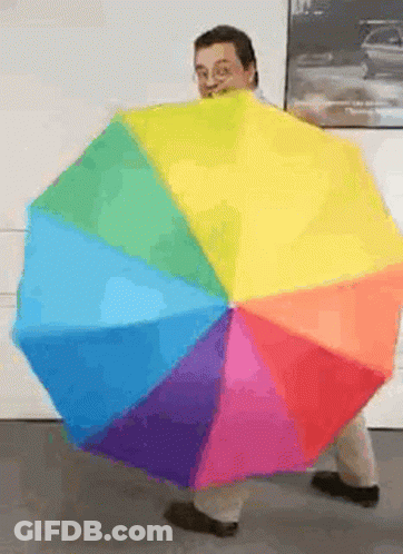 A Man Is Holding A Rainbow Colored Umbrella In Front Of Him GIF