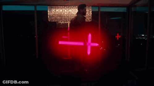 A Man Is Holding A Red Cross In Front Of A Crystal Chandelier GIF