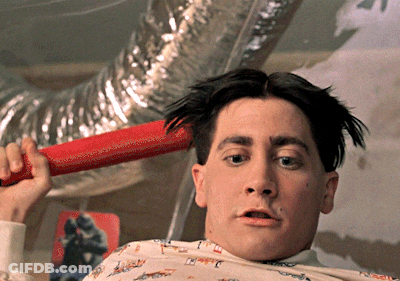 A Man Is Holding A Red Object In Front Of His Head With A Picture Of A Man On The Wall In The Background GIF